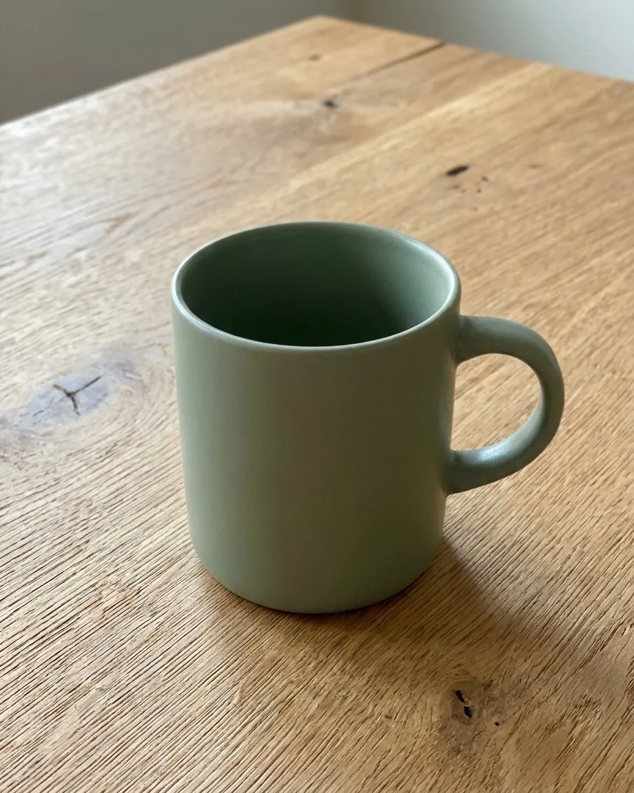 Sage green ceramic mug on a raw oak wooden table